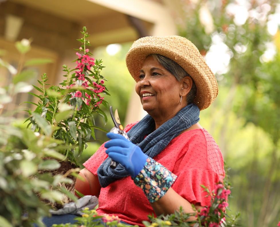 Older woman in a straw hat pruning flowers in her garden
