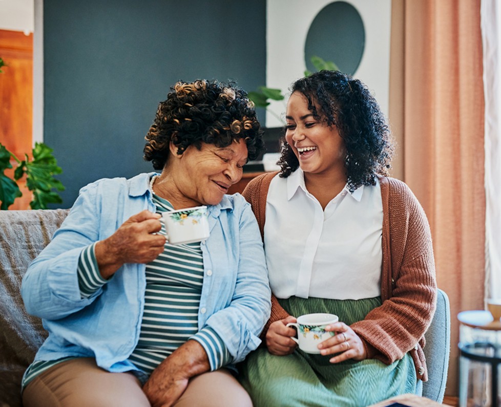 Older woman and her caregiver laughing together over tea at home
