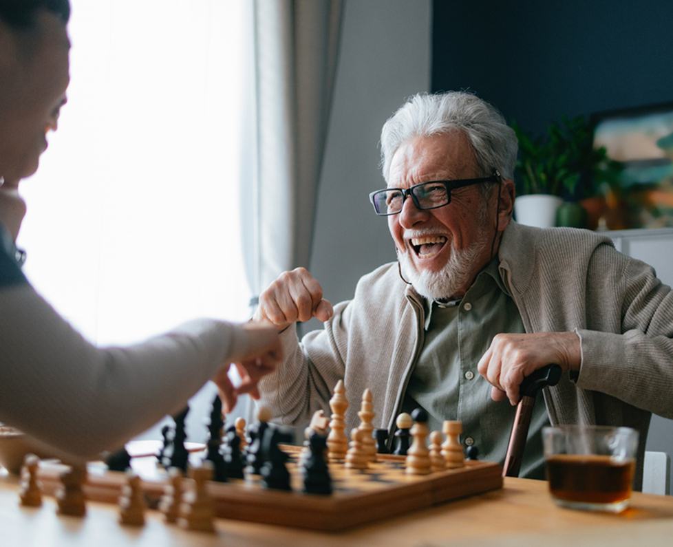 Older man laughing over a chessboard during a game with a visitor